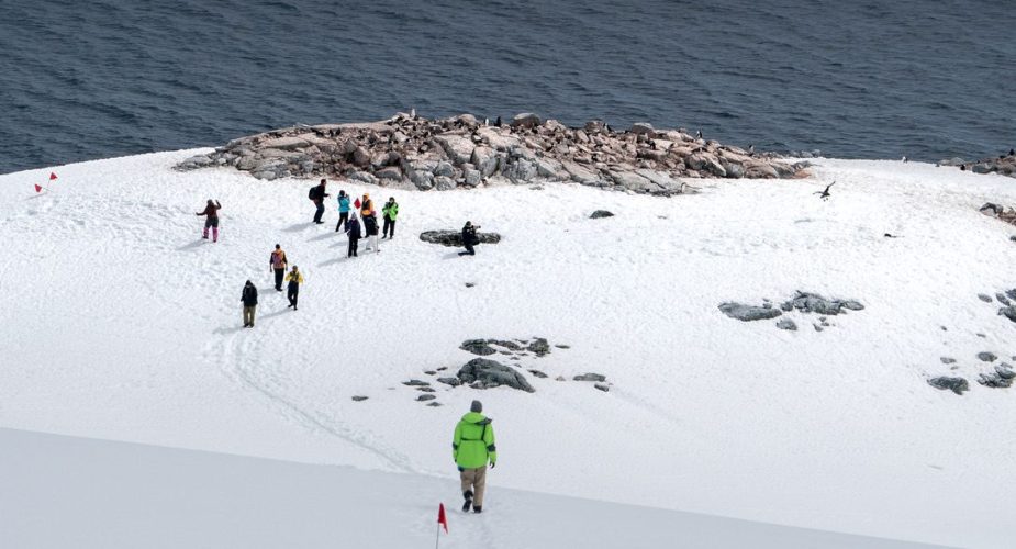 People hiking down a snowy mountain towards the water