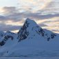 Snowy mountains in the shadows of a warm cloudy sky.