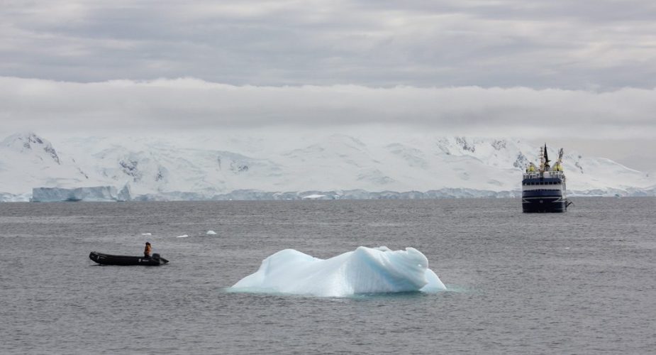 An iceberg and two boats, one large and one small, in the Arctic