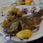 A cooked whole fish on a plate with potatoes and lemon garnish.