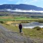 Wendy in Iceland in surrounded by fields, water and a mountain.