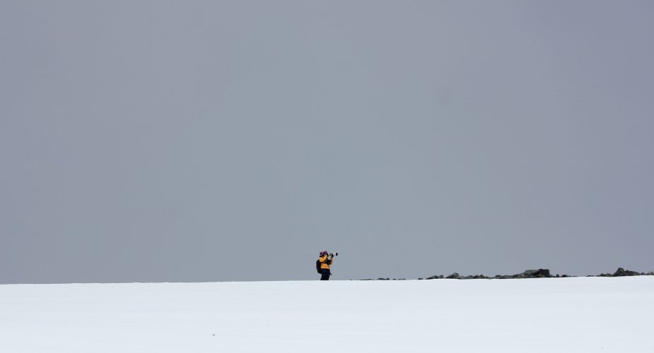 A person photographing with a telephoto lens on a grey day in Antarctica