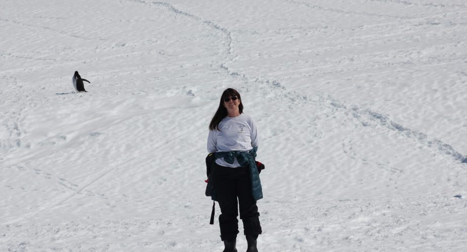 Wendy posing on the snow with a penguin in the background